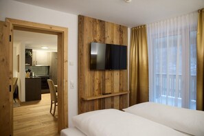 A hotel room with a bed, a television mounted on a wooden panel wall, a window with curtains, and a view of the outside. - Suite with outdoor sauna (Gaschurn)