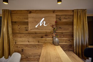 Ein Empfangsbereich mit einer Holzwand, einem großen Buchstaben 'h', einer Vase mit Blumen und einem Holztisch.