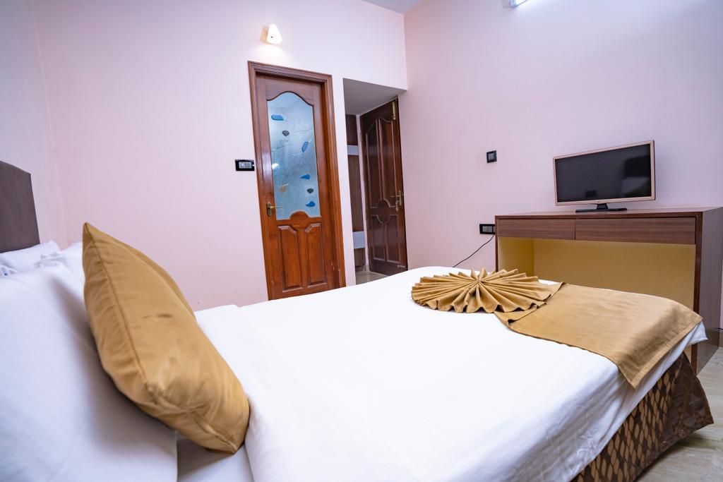 A hotel room with a bed, a television on a wooden cabinet, and a door with a decorative glass panel.