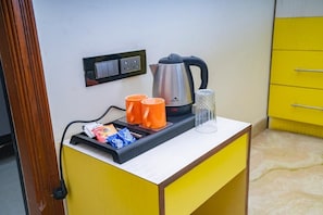 Une petite kitchenette équipée d’une bouilloire, de deux tasses oranges et d’un récipient en verre, le tout posé sur un comptoir jaune.