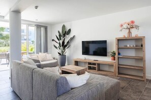 Ein modernes Wohnzimmer mit einem grauen Sofa, einem Flachbildfernseher, einem Holztisch und einer Topfpflanze.
