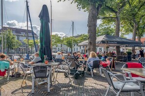 An outdoor café with tables and chairs, a stroller, and umbrellas. - Holiday home with 2 bedrooms (Oude-Tonge)