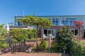 Ein modernes Gebäude mit Ziegelverkleidung, großen Fenstern und einer Terrasse mit Sitzgelegenheiten im Freien.