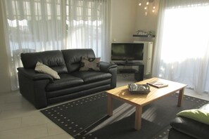 Ein Wohnzimmer mit einem schwarzen Ledersofa, einem Holztisch und einem Fernseher.