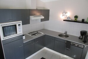Una cucina moderna con mobili grigi, un forno a microonde integrato, un piano cottura a gas, un lavello e una macchina da caffè.