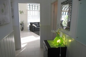 Ein Flur mit einem schwarzen Konsolentisch, einer grünen Vase mit Blumen und einem dekorativen Spiegel an der Wand.