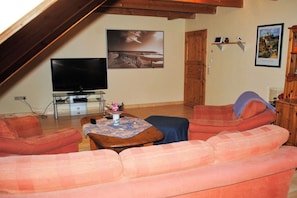 Ein Wohnzimmer mit Fernseher, Sofa und einem Tisch mit einer Vase.
