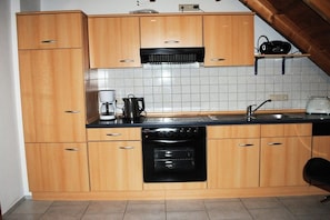 A kitchen with wooden cabinets, a black oven, a coffee maker, and a toaster. - Holiday apartment with 2 bedrooms (Norden)