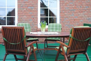 A wooden table with four chairs, a vase with flowers, and a brick wall with windows. - Holiday apartment with 2 bedrooms (Norden)