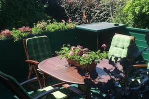Een terras met een ronde tafel, twee stoelen en een bloempot.