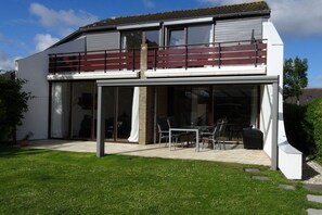 A modern two-story house with a balcony, large sliding glass doors, and a patio area. - Holiday home with 2 bedrooms (Brouwershaven)