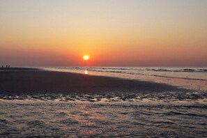 A beach scene with the sun setting over the water, creating a calm atmosphere. - Holiday home with 2 bedrooms (Brouwershaven)