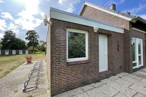 Ein Backsteinhaus mit weißer Tür, einem Fenster und einer Leuchte an der Außenwand.