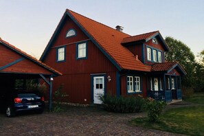 A two-story house with a red roof, a garage, and a car parked in front. - Holiday home in Eschede with swimming pool (Eschede)