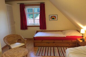 A bedroom with a wooden bed, a chair, a window with curtains, and a rainbow picture on the wall. - Holiday home in Eschede with swimming pool (Eschede)