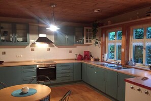 A kitchen with teal cabinets, a wooden ceiling, and a window with a view of greenery. - Holiday home in Eschede with swimming pool (Eschede)