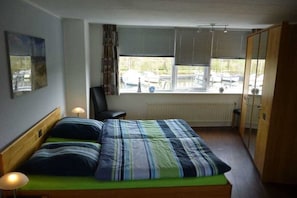 Ein Schlafzimmer mit einem Bett, einem Sessel, einer Heizung und einem Fenster mit Blick auf parkende Autos.