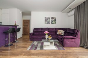 A modern living room with a purple sofa, a glass coffee table, and a small bar area with stools. - Lumina 3-Room Apt with Balcony & City View (Warszawa)