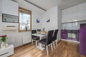 Une cuisine moderne avec un coin repas, comprenant une table blanche dressée pour deux personnes, des chaises noires et un meuble violet.