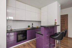 Une cuisine moderne avec des armoires violettes, un plan de travail noir et un four encastré.