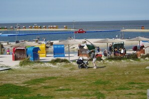 Eine Strandpromenade mit einem Steg, Strandstühlen und einigen Personen.