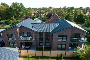A two-story house with a sloped roof, a balcony, and a fenced backyard. - Holiday apartment JAN on the North Sea dike (Butjadingen)