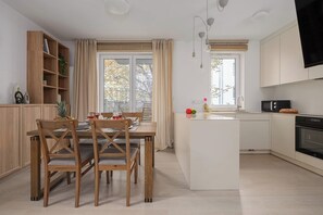 Une cuisine moderne avec un îlot central, des chaises en bois, une table à manger et un téléviseur fixé au-dessus de l’îlot.