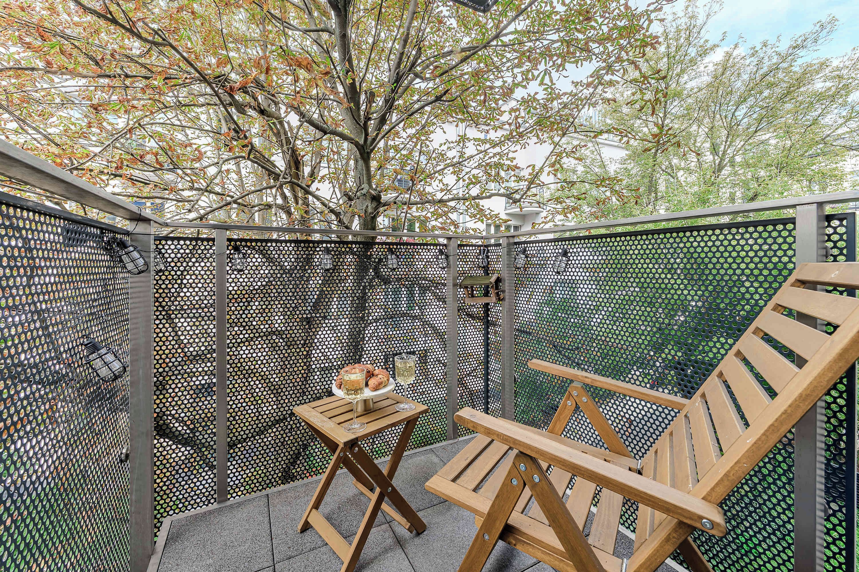 Un patio con una mesa y dos sillas de madera, un árbol y una cerca con diseños circulares.