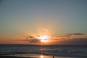 Ein Sonnenuntergang über dem Meer mit der Silhouette einer Person, die am Strand steht.