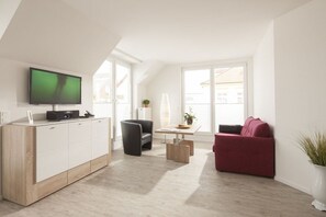 Ein modernes Wohnzimmer mit einem Flachbildfernseher, einem Holzschrank, einem schwarzen Sessel, einem roten Sofa und einem kleinen Tisch mit einer Pflanze.
