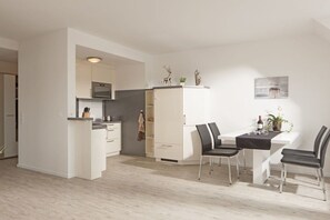 Eine moderne Küche mit weißen Schränken, einem Essbereich mit Tisch und Stühlen sowie einem kleinen Schrank mit Dekoration.