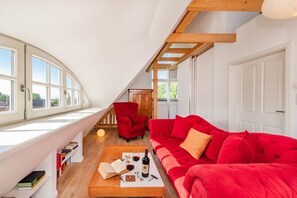 A cozy living room with a red sofa, a wooden coffee table, and a red armchair. There is a bookshelf with books and a bottle of wine on the table. - The Beautiful House in Sellin—Pure Relaxation with a Sauna and Fireplace (Sellin)