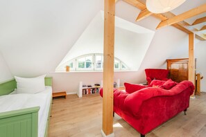 Ett rum med ett sluttande tak, en säng med en grön sänggavel, en röd soffa och ett träskåp.