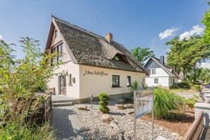 Een traditioneel gebouw met een schuin dak, een bord waarop 'Unser Schlafhaus' staat, en een geplaveid entreegebied met een kleine tuin.