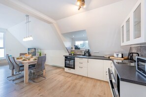 Een moderne keuken met een eethoek, met een centraal kookeiland, een ingebouwde oven en een groot raam dat natuurlijk licht toelaat.