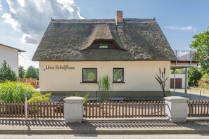 Ein traditionelles Gebäude mit einem Strohdach, einem kleinen Fenster und einem Schild mit der Aufschrift 'Unser Schlafhaus'.
