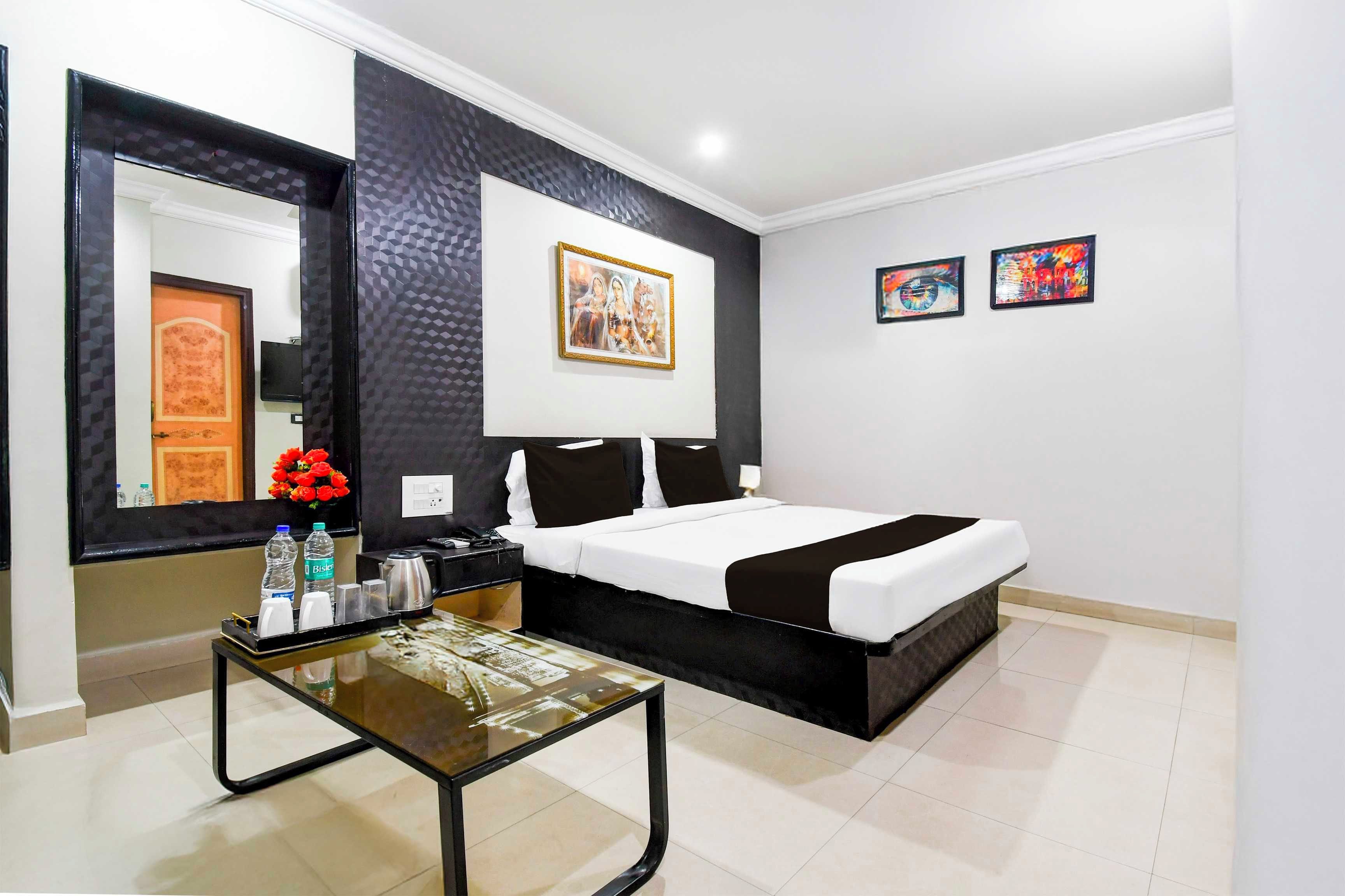 Quarto de hotel com cama, mesa de cabeceira com abajur, espelho e obras de arte na parede.