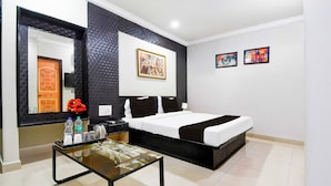 A hotel room with a bed, a bedside table with a lamp, a mirror, and artwork on the wall. - Collection O Railway Station (Raipur)