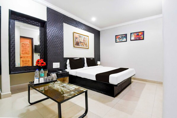 Quarto de hotel com cama, mesa de cabeceira com abajur, espelho e obras de arte na parede.