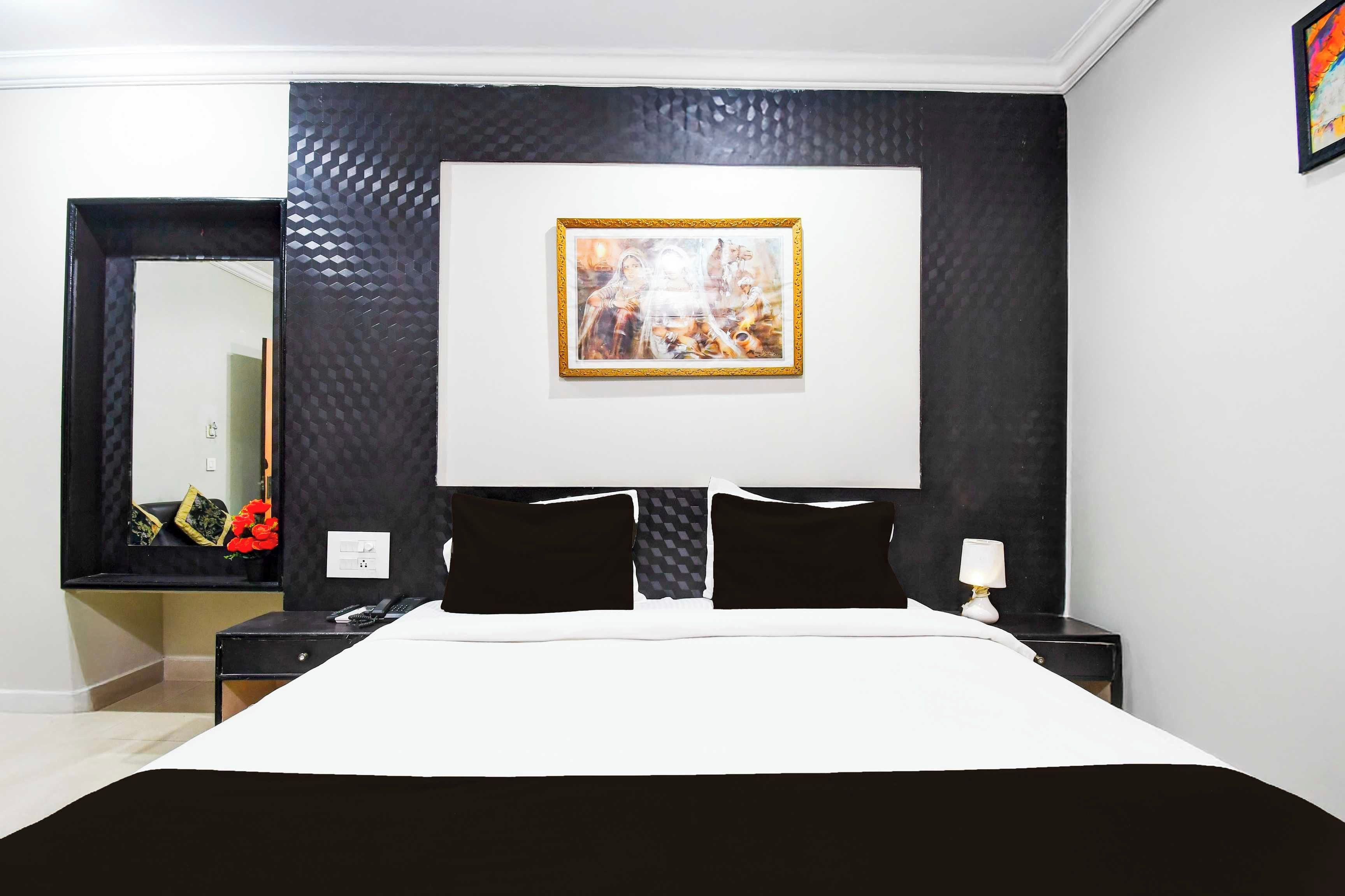 A hotel room with a large bed, a nightstand, a lamp, and a framed picture on the wall.