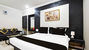 A hotel room with a large bed, a sofa, a coffee table, and a painting on the wall. - Collection O Railway Station (Raipur)