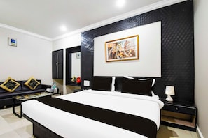 A hotel room with a large bed, a sofa, a coffee table, and a painting on the wall. - Collection O Railway Station (Raipur)