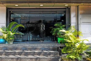 Una entrada de edificio con puerta de cristal, escalones que conducen a ella y plantas en macetas a ambos lados.