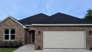 Une maison d’habitation avec une façade en briques, un garage et une pelouse bien entretenue.