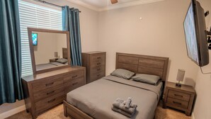 Une chambre à coucher comprenant un lit, une commode, une table de chevet, un miroir et un téléviseur.