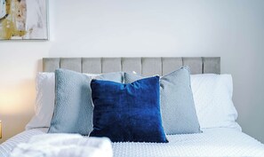 This cozy bed setup features a grey tufted headboard dressed with white linens, two textured light-blue pillows, and a prominent dark blue velvet accent cushion. - 19 Colwick House, Rotherham (South Yorkshire)