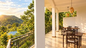 Un balcone con vista su una zona boschiva, un tavolo con sedie e un lampadario.