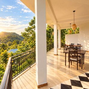 Ein Balkon mit Blick auf ein bewaldetes Gebiet, einem Esstisch mit Stühlen und einer hängenden Leuchte.