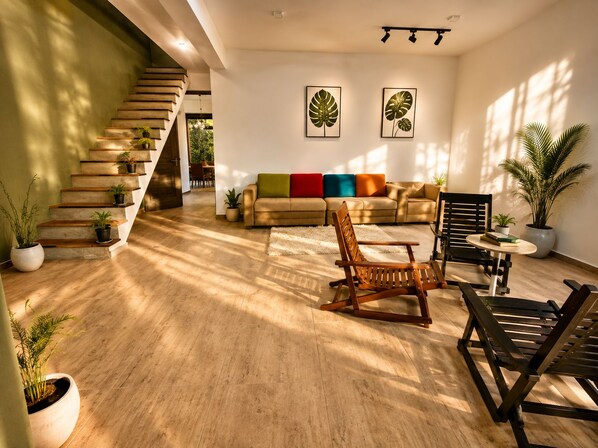 A modern living room with a staircase, a sofa set, and multiple potted plants.
