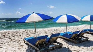 Ein Strand mit blauen und weißen Streifen-Schirmen und Holzliegen.